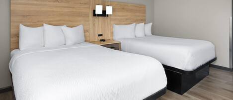 A hotel room with two beds, a wooden headboard, bedside tables, and wall-mounted lighting.