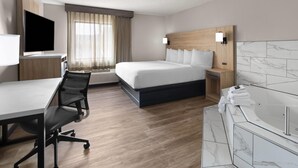 Habitación de hotel con cama, escritorio y silla, televisor, baño con bañera y ventana con cortinas.