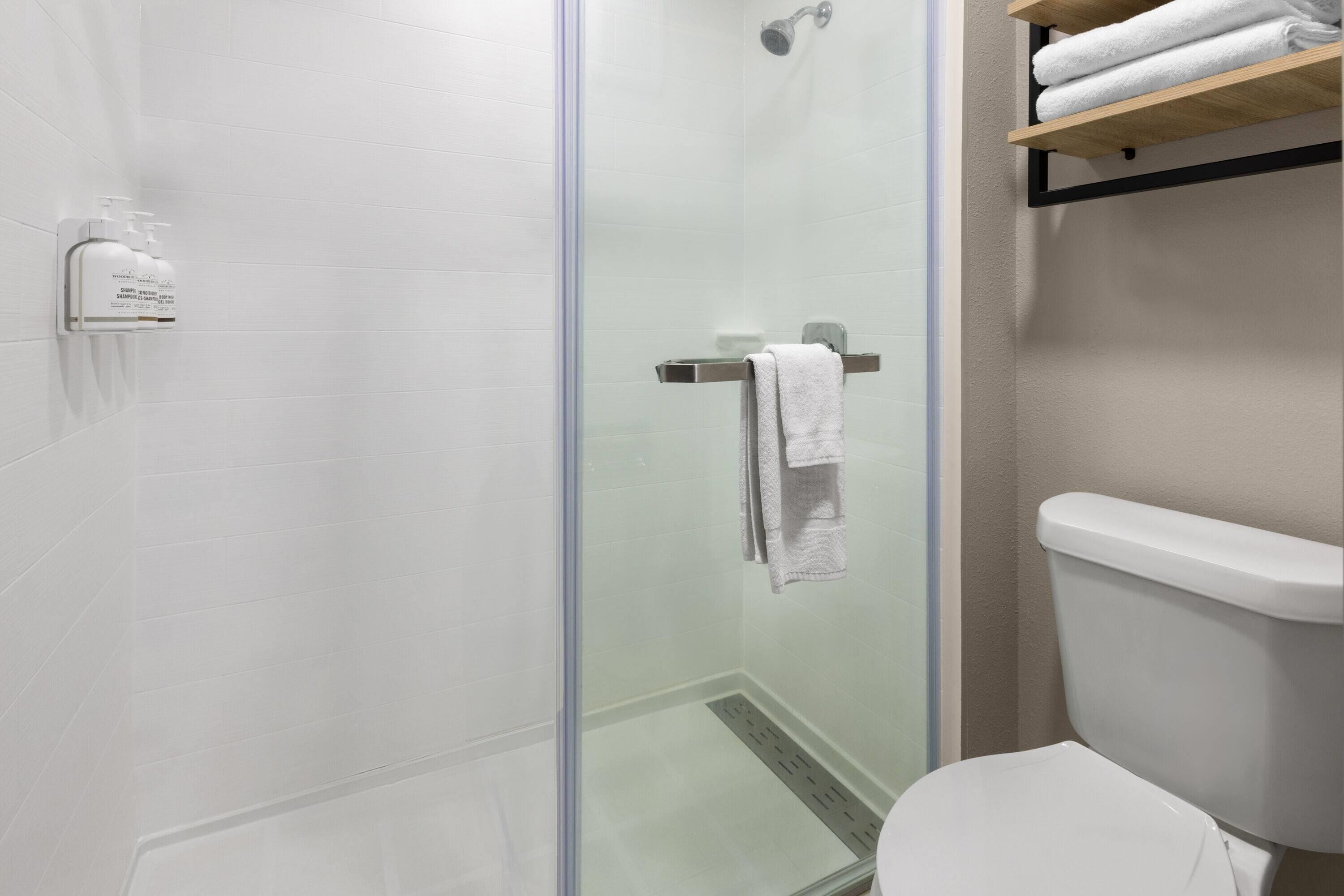 A modern bathroom with a glass-enclosed shower, a toilet, and a shelf with folded towels.