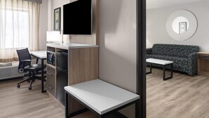 Una habitación de hotel moderna con escritorio, silla, sofá y televisor de pantalla plana montado en la pared.