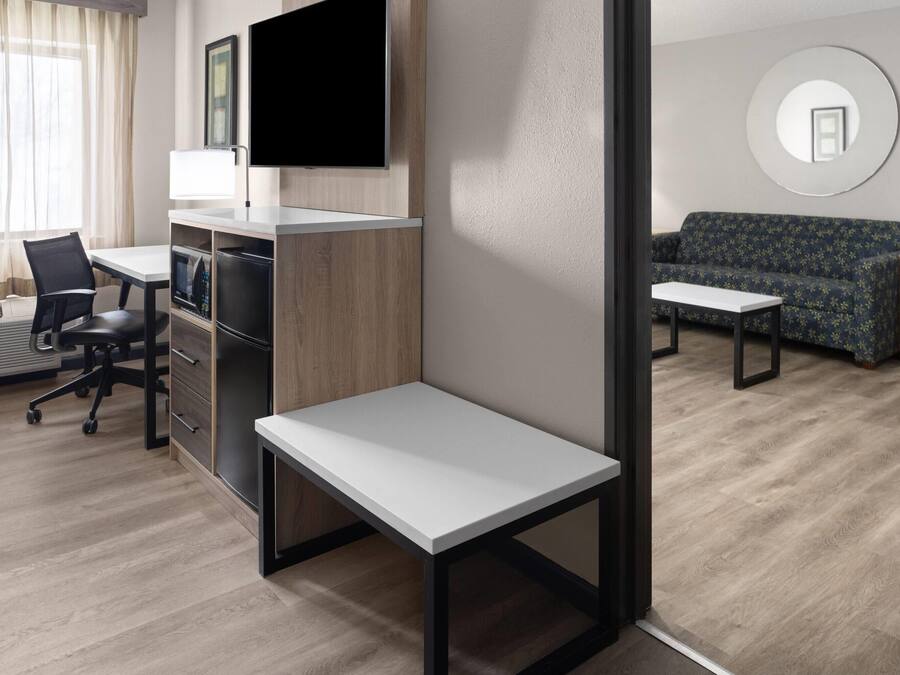 A modern hotel room with a desk, chair, sofa, and a flat-screen TV mounted on the wall.