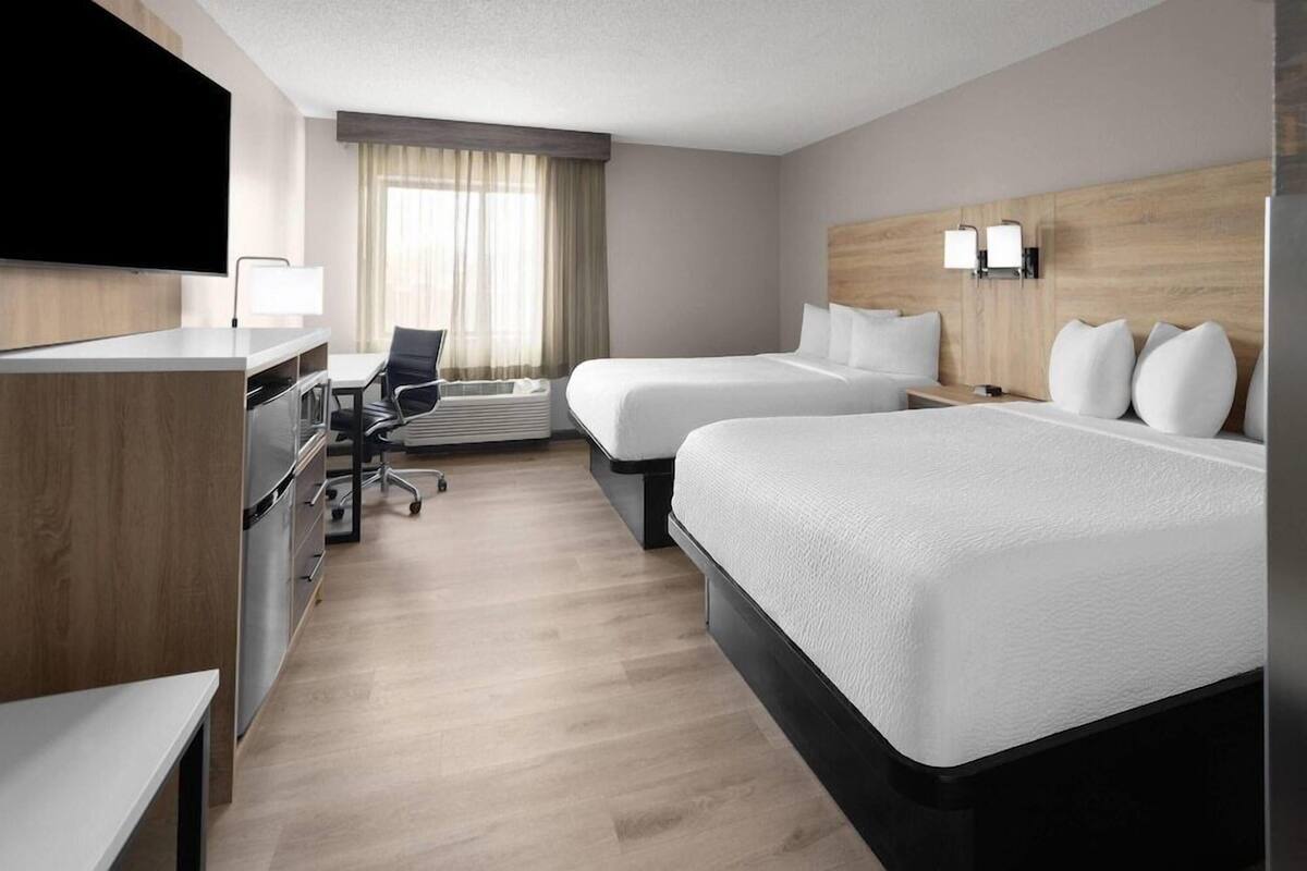 Ein Hotelzimmer mit zwei Betten, einem Schreibtisch, einem Sessel, einem Fernseher und einem Fenster mit Vorhängen.