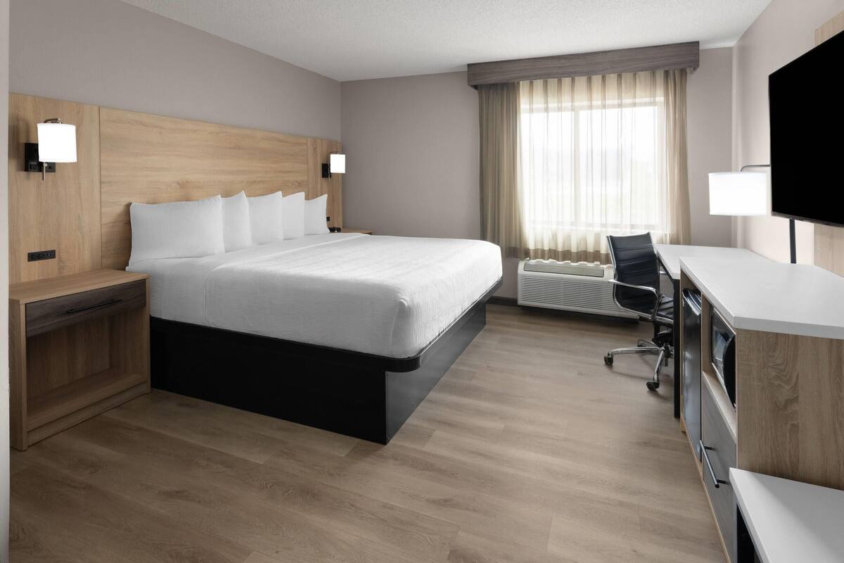 Ein Hotelzimmer mit einem großen Bett, einem Schreibtisch, einem Stuhl und einem Fernseher.
