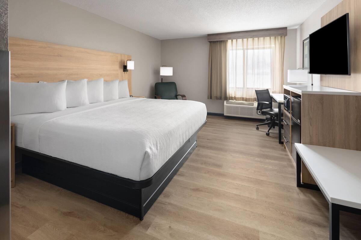 Ein Hotelzimmer mit einem großen Bett, einem Schreibtisch mit Stuhl, einem Flachbildfernseher und einem Fenster mit Vorhängen.