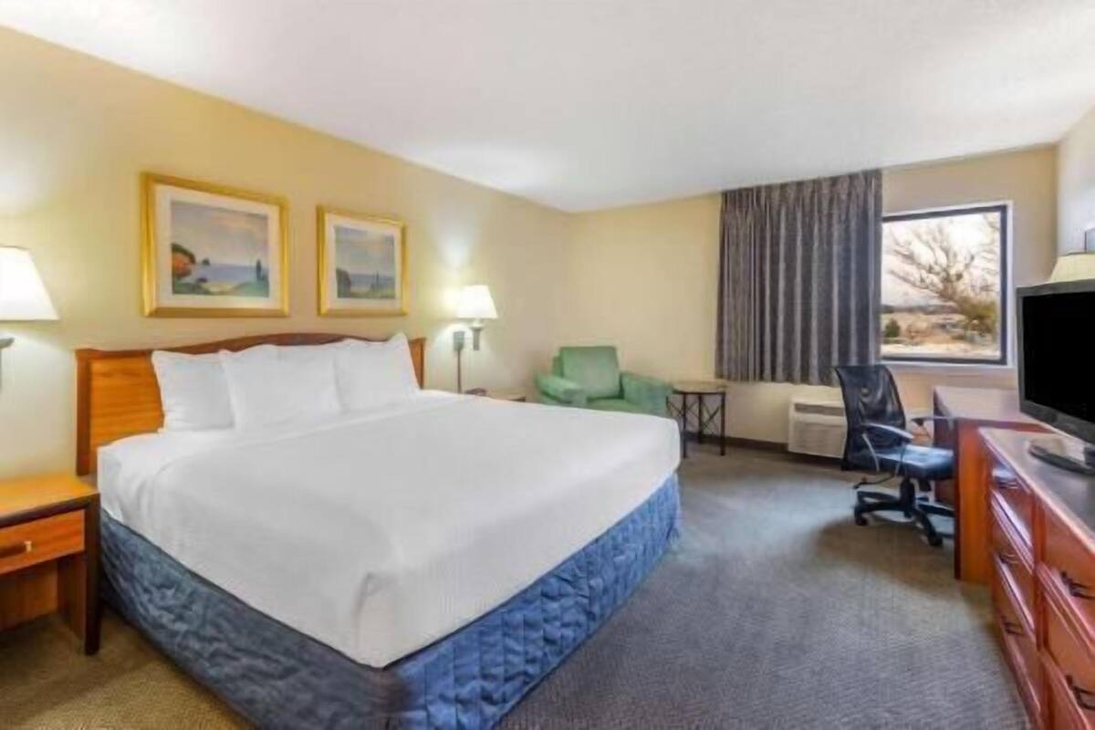 Ein Hotelzimmer mit einem großen Bett, einem Schreibtisch, einem Sessel, einem Fernseher und zwei gerahmten Bildern an der Wand.