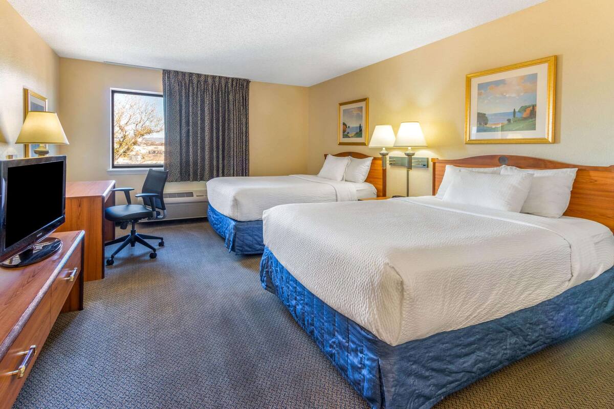 Ein Hotelzimmer mit zwei Betten, einem Schreibtisch mit Fernseher, einem Sessel und zwei Lampen.