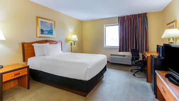 A hotel room with a bed, bedside tables, a desk with a television, an air conditioning unit, and a window with curtains.