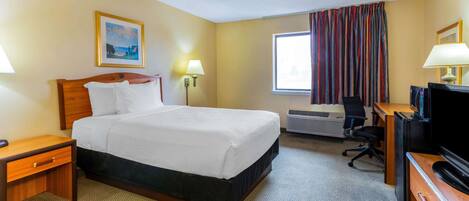 Una habitación de hotel con cama, mesitas de noche, un escritorio con televisor, unidad de aire acondicionado y ventana con cortinas.