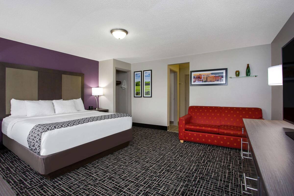 A hotel room with a large bed, a red sofa, a desk, and a patterned carpet.