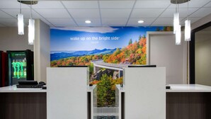 A reception desk with a scenic wall mural, a Monster energy drink cooler, and a modern pendant light fixture. - La Quinta Inn & Suites by Wyndham Roanoke Salem (Salem)