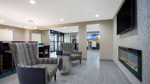 A modern lobby with patterned chairs, a fireplace, and a large TV on the wall. - La Quinta Inn & Suites by Wyndham Roanoke Salem (Salem)