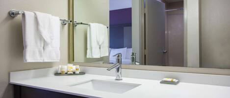 A bathroom with a white sink, a mirror, and two towels hanging on a towel rack.