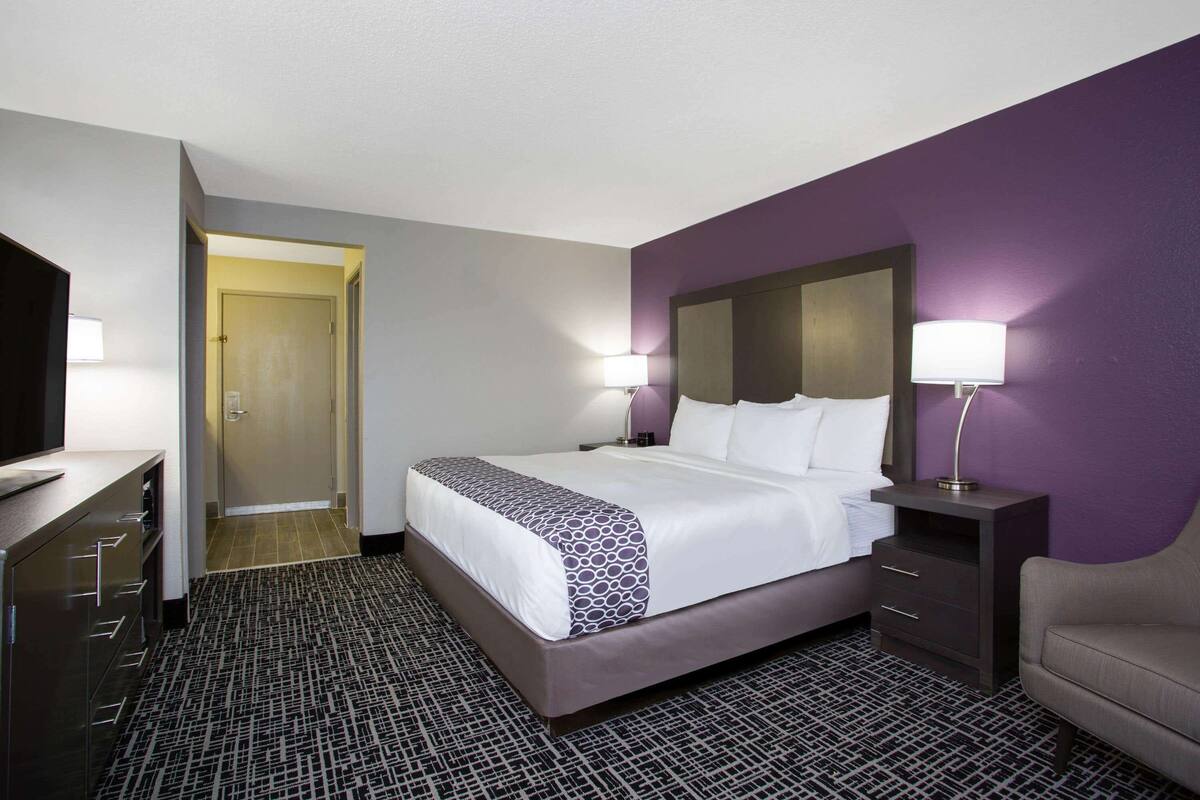 A hotel room with a bed, a desk, a chair, and a TV.