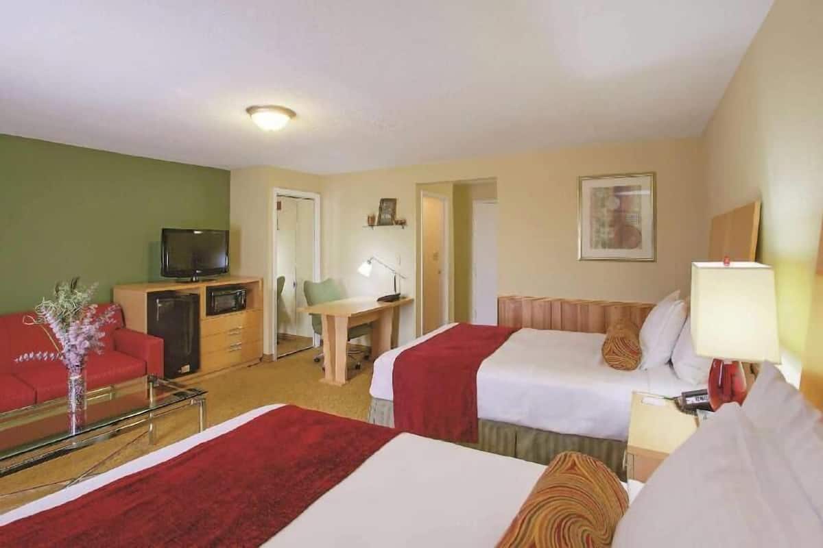 A hotel room with two beds, a desk, a television, and a small kitchenette.
