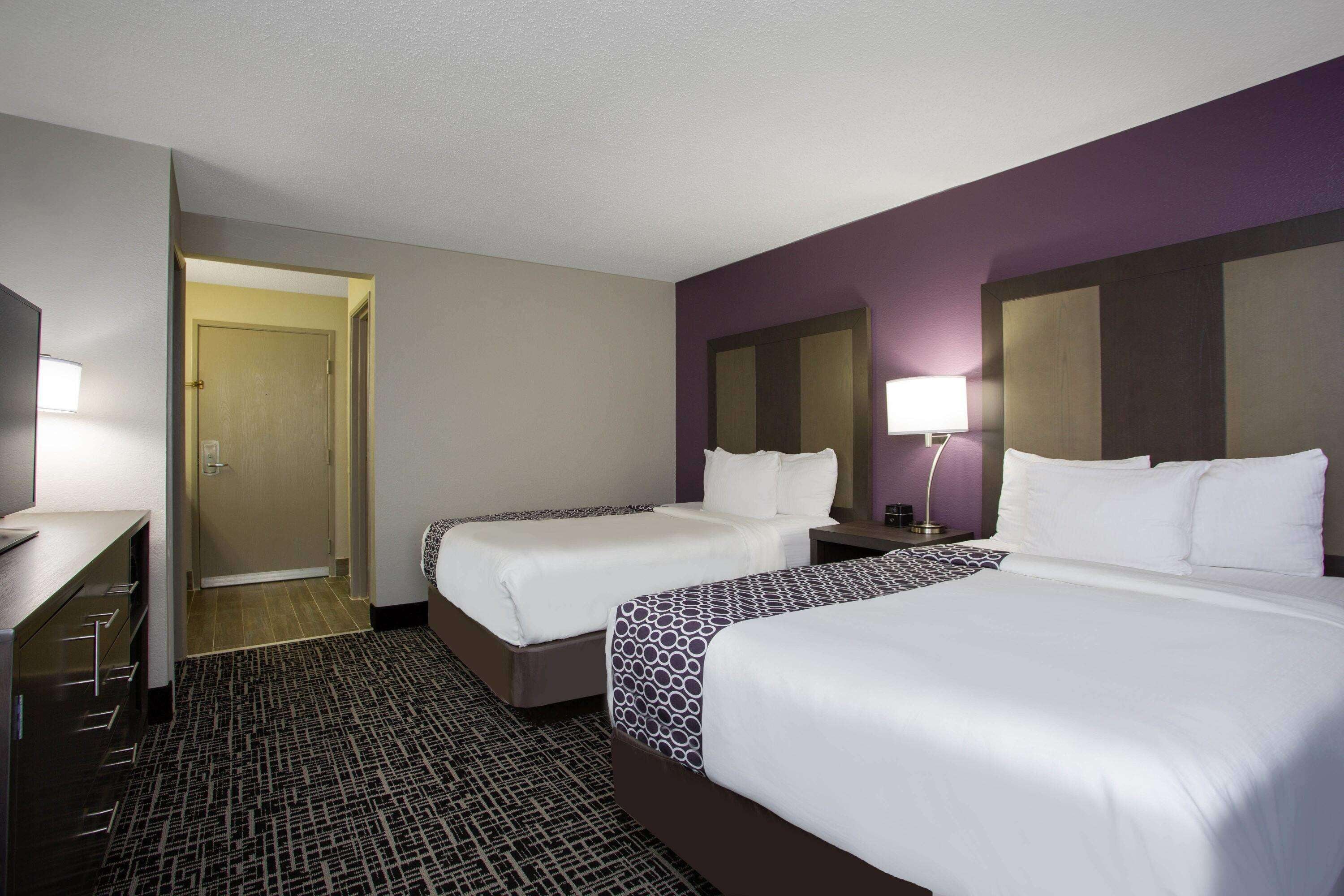 A hotel room with two beds, a desk, and a door leading to a hallway.