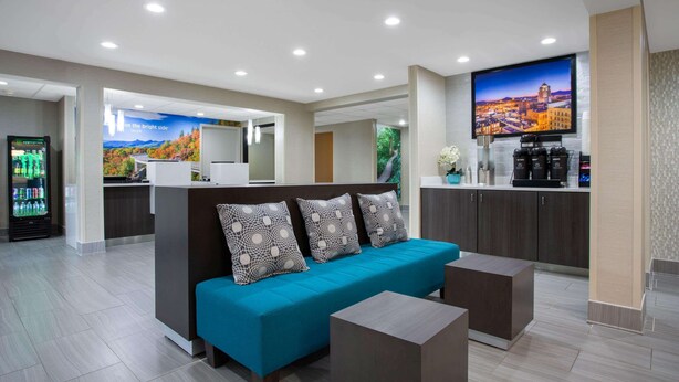 A modern hotel lobby with a sofa, a coffee station, and a refrigerator. - La Quinta Inn & Suites by Wyndham Roanoke Salem (Salem)