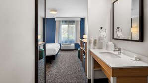 Ein Hotelzimmer mit Bett, Schreibtisch, Badezimmer mit Waschbecken und Spiegel sowie einem Fenster mit Vorhängen.