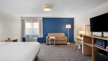 Een hotelkamer met een bed, een bank, een bureau met een computer, een televisie en een magnetron.