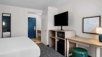 A hotel room with a bed, a desk with a TV, a microwave, and a trash bin.