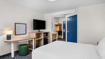 A hotel room with a bed, a desk with a TV, a microwave, and a trash bin.