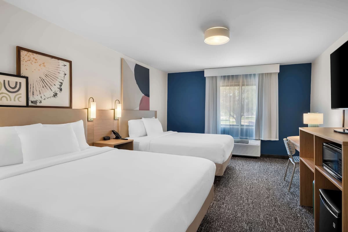 A hotel room with two beds, a desk, a TV, and a window with curtains.