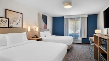 A hotel room with two beds, a desk, a TV, and a window with curtains.