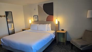A hotel room with a large bed, two bedside tables, a chair, a wall-mounted artwork, and a mirror.