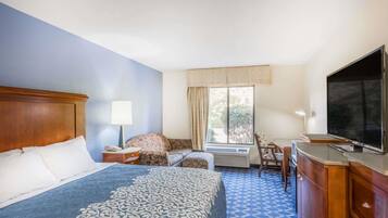 A hotel room with a bed, a desk, a chair, a television, and a window with curtains.