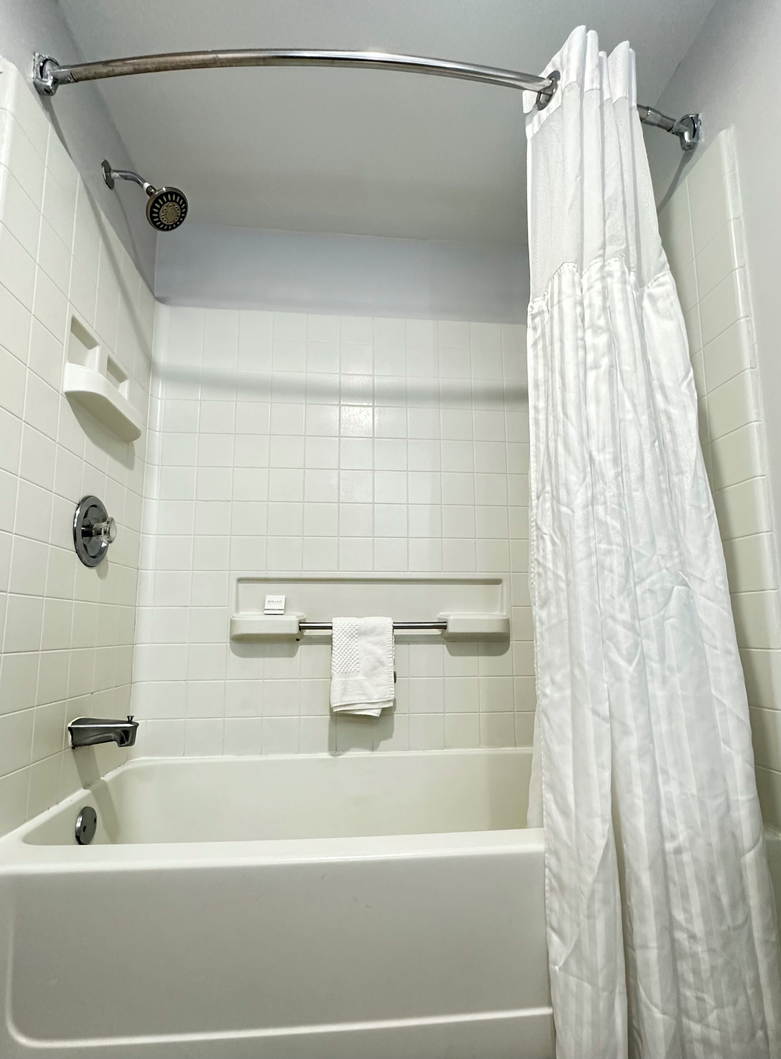 A white bathtub with a showerhead, a towel rack with a towel, and a white shower curtain.