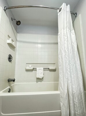 A white bathtub with a showerhead, a towel rack with a towel, and a white shower curtain.