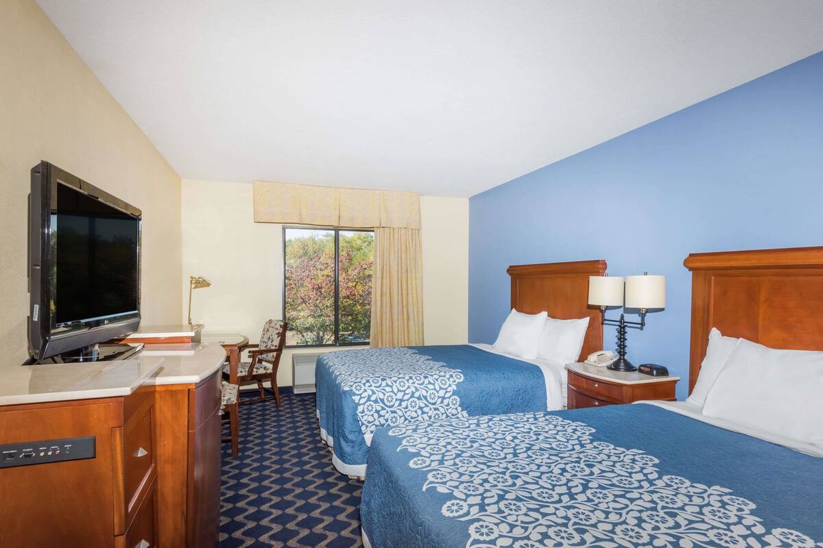 Habitación de hotel con dos camas, televisión, escritorio y ventana con vista a árboles.