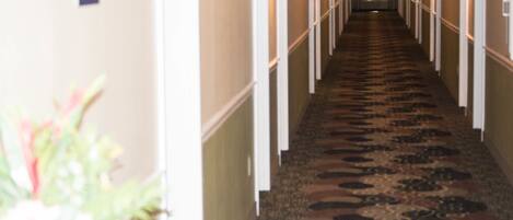 Un pasillo de hotel con piso alfombrado, paredes blancas y una puerta al final.