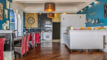A modern restaurant interior with a bar area, wooden flooring, and red upholstered chairs.