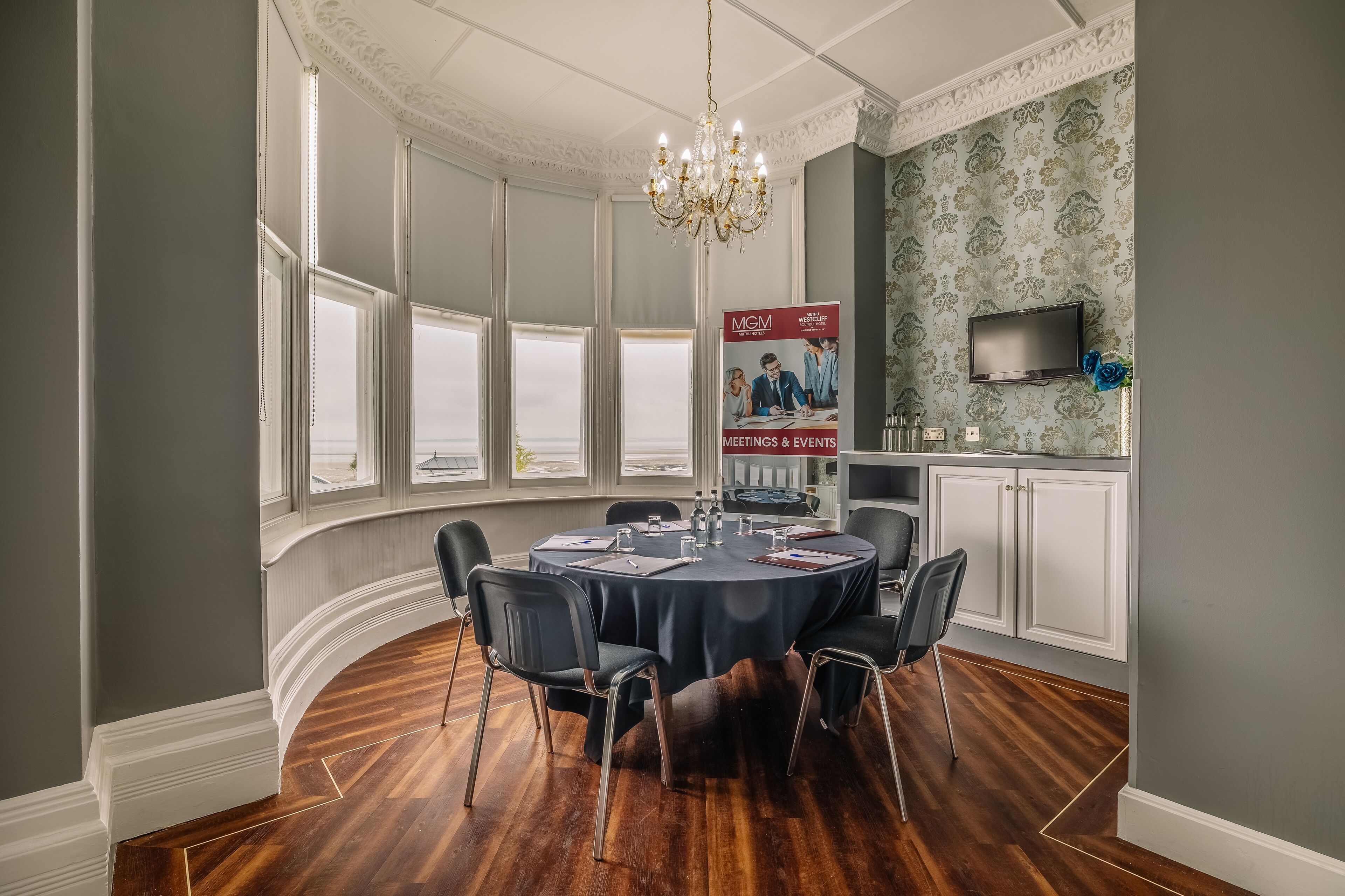 A conference room with a round table, chairs, a chandelier, and a poster on the wall.