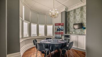 A conference room with a round table, chairs, a chandelier, and a poster on the wall.