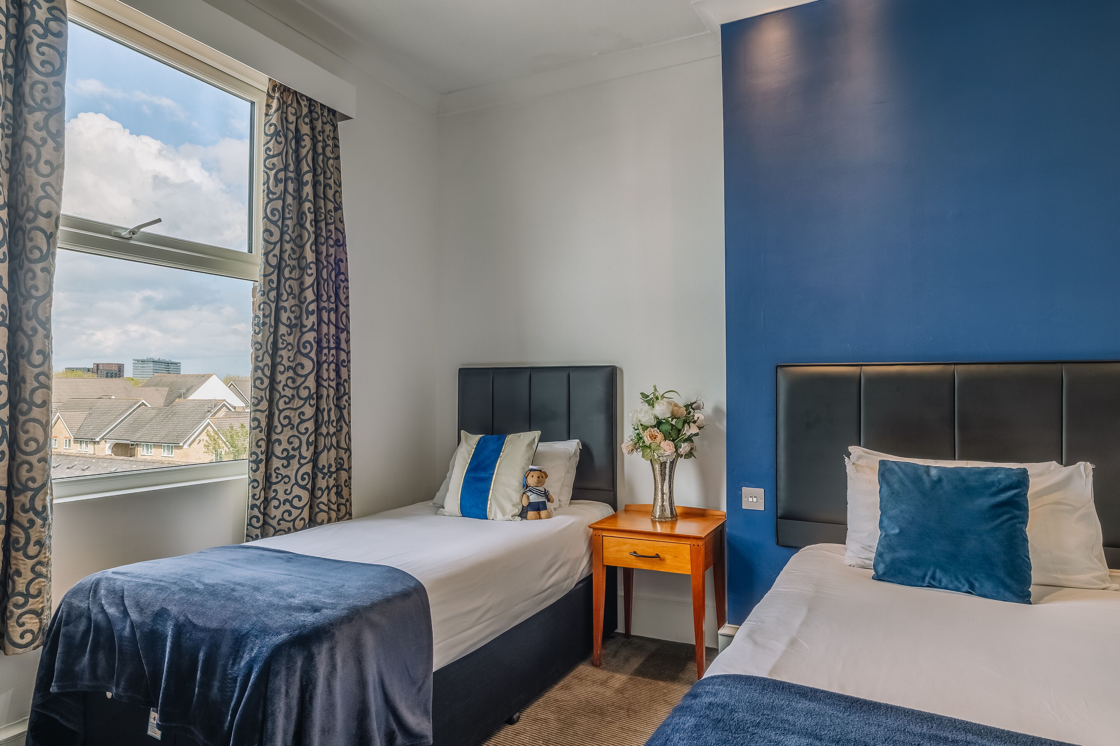 A hotel room with two beds, a nightstand, and a window with curtains.