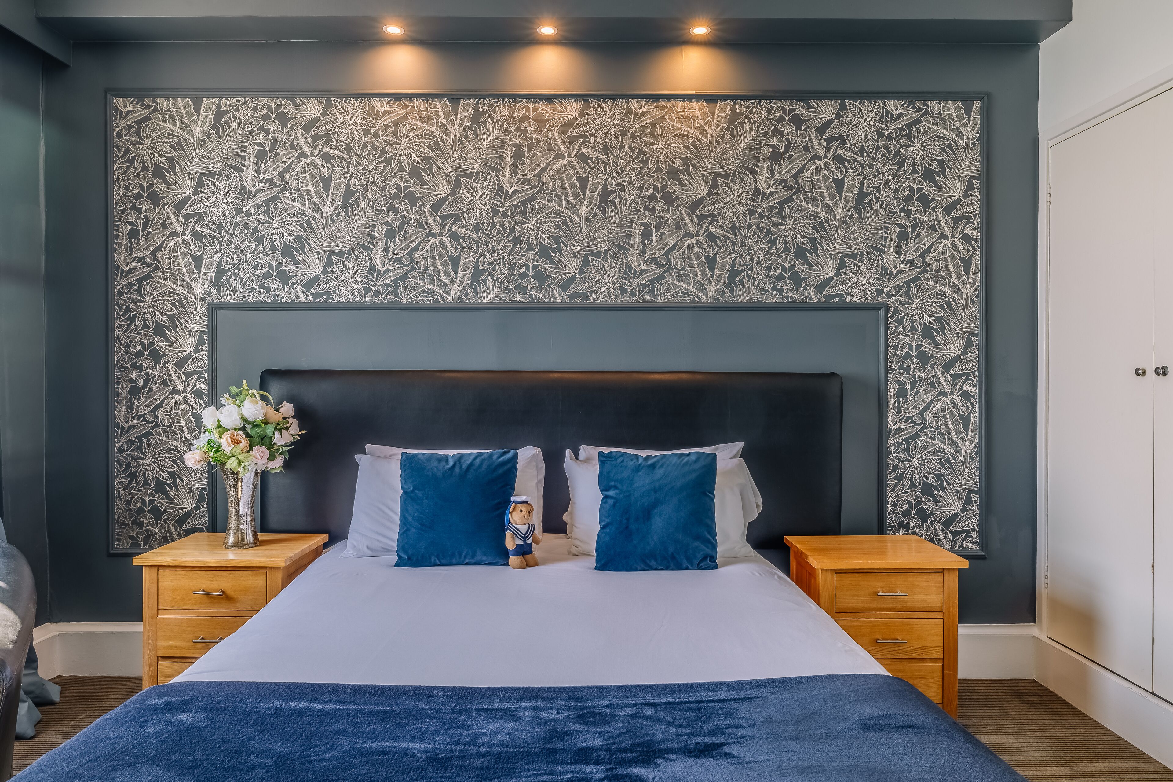 A bedroom with a large bed, two nightstands, a wooden dresser, and a floral-patterned wall.