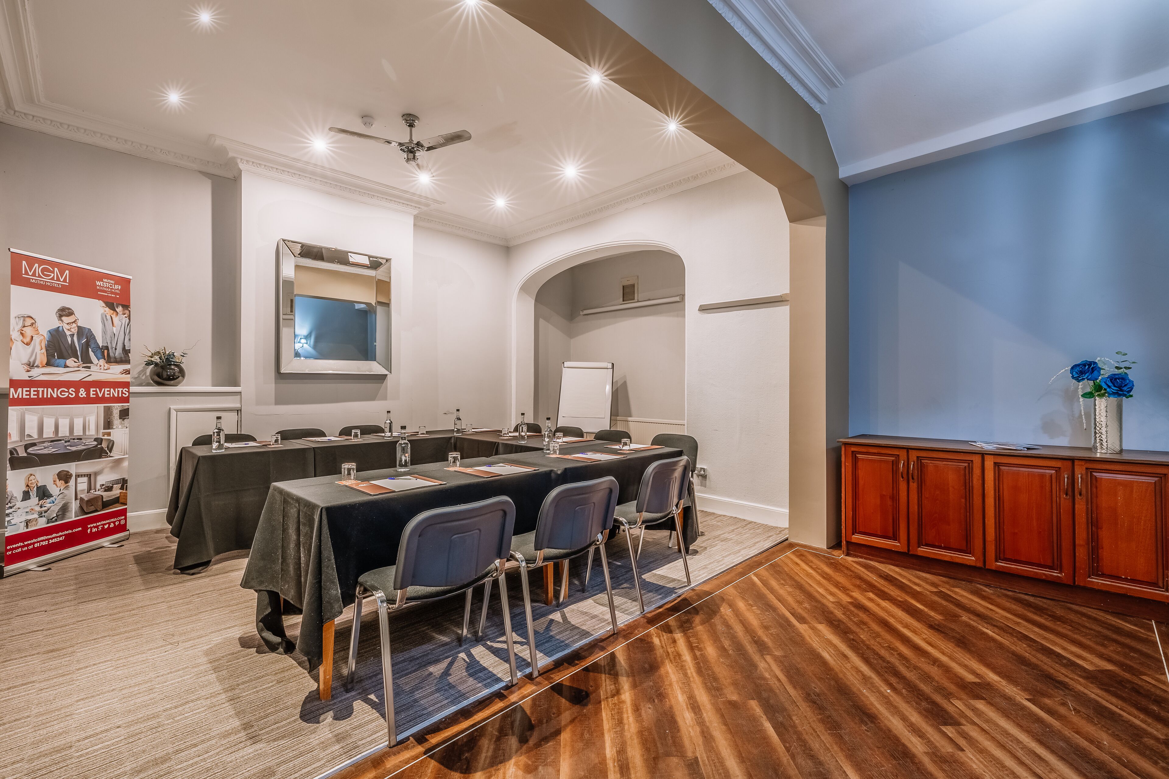 A conference room with a long table, chairs, a whiteboard, and a ceiling fan.