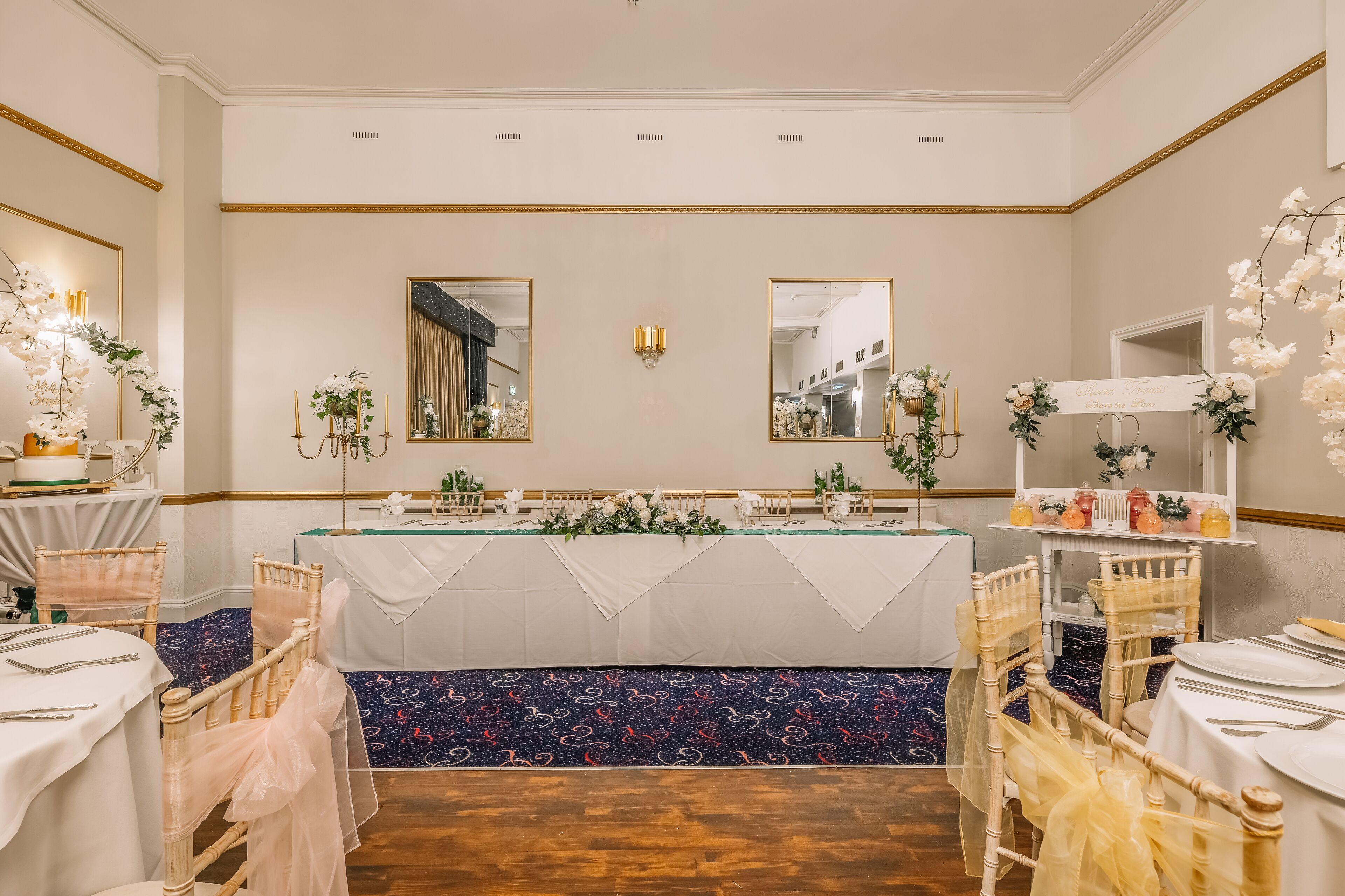 A banquet hall with a long table, white tablecloths, and floral centerpieces.