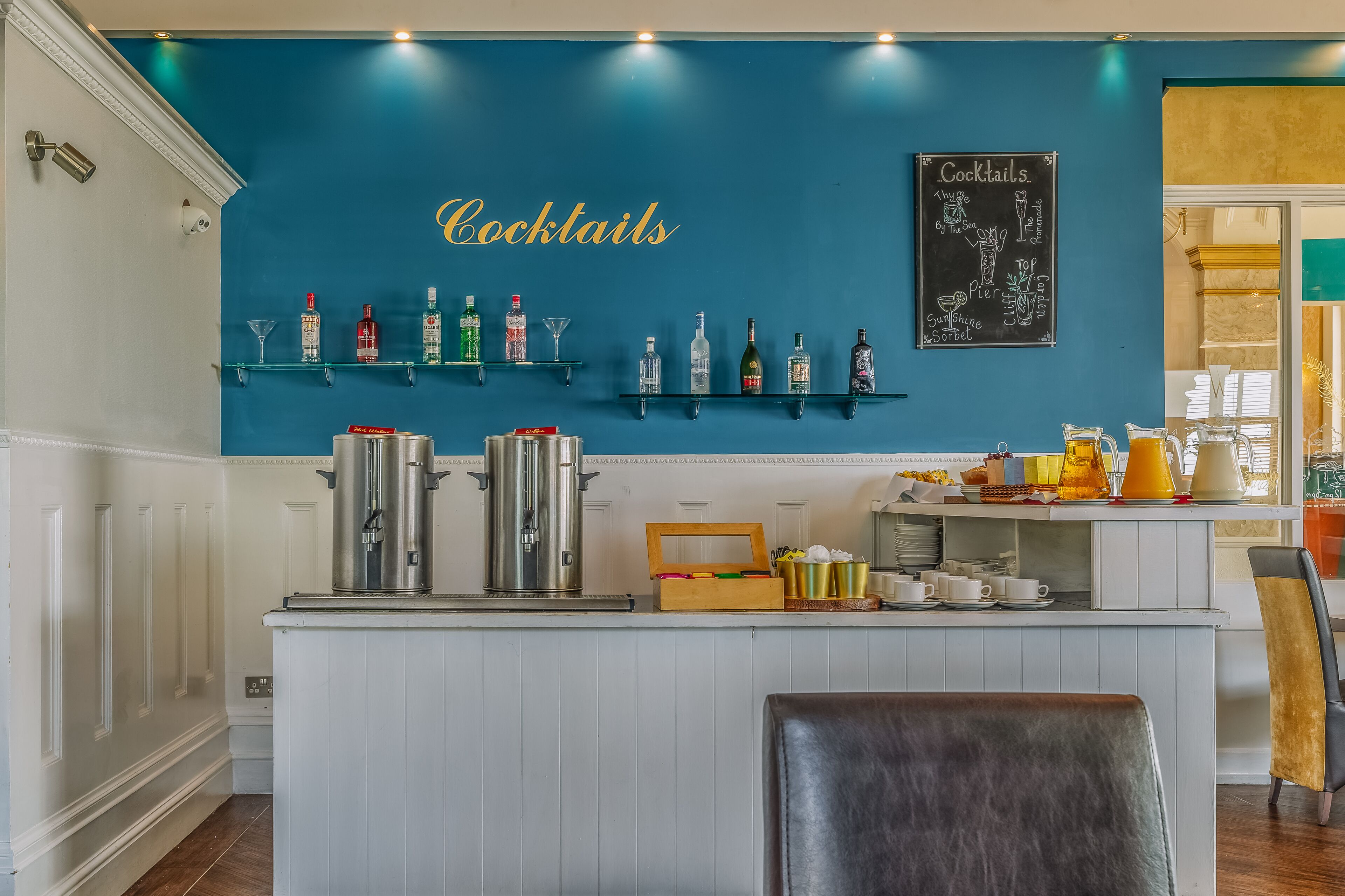 Zona de bar con pared azul, estantes llenos de botellas, un menú en la pizarra y una barra con diversos artículos.