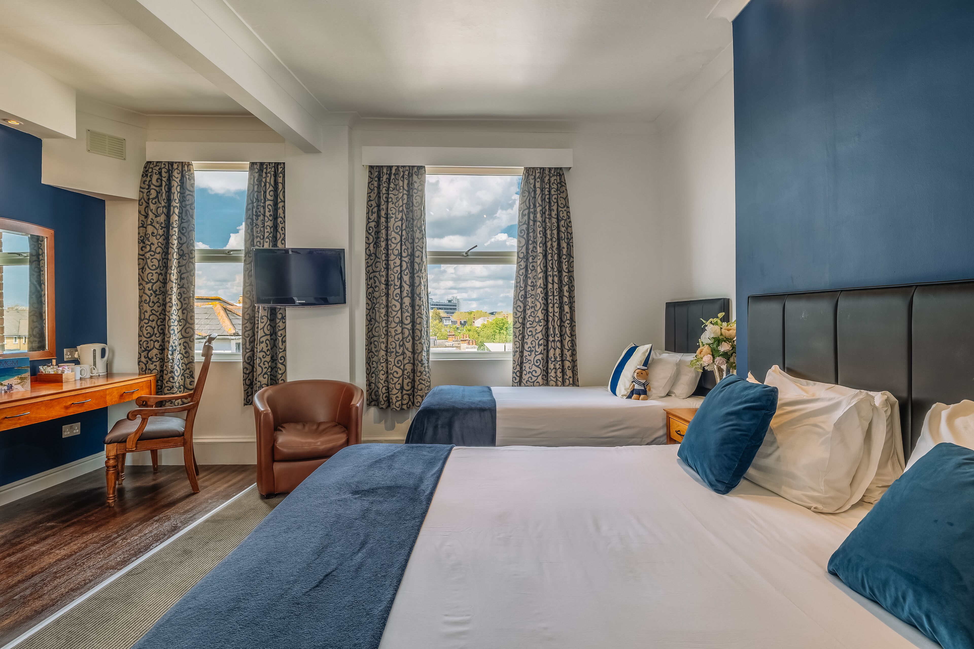 A hotel room with a bed, a desk, a chair, a television, and a window with curtains.