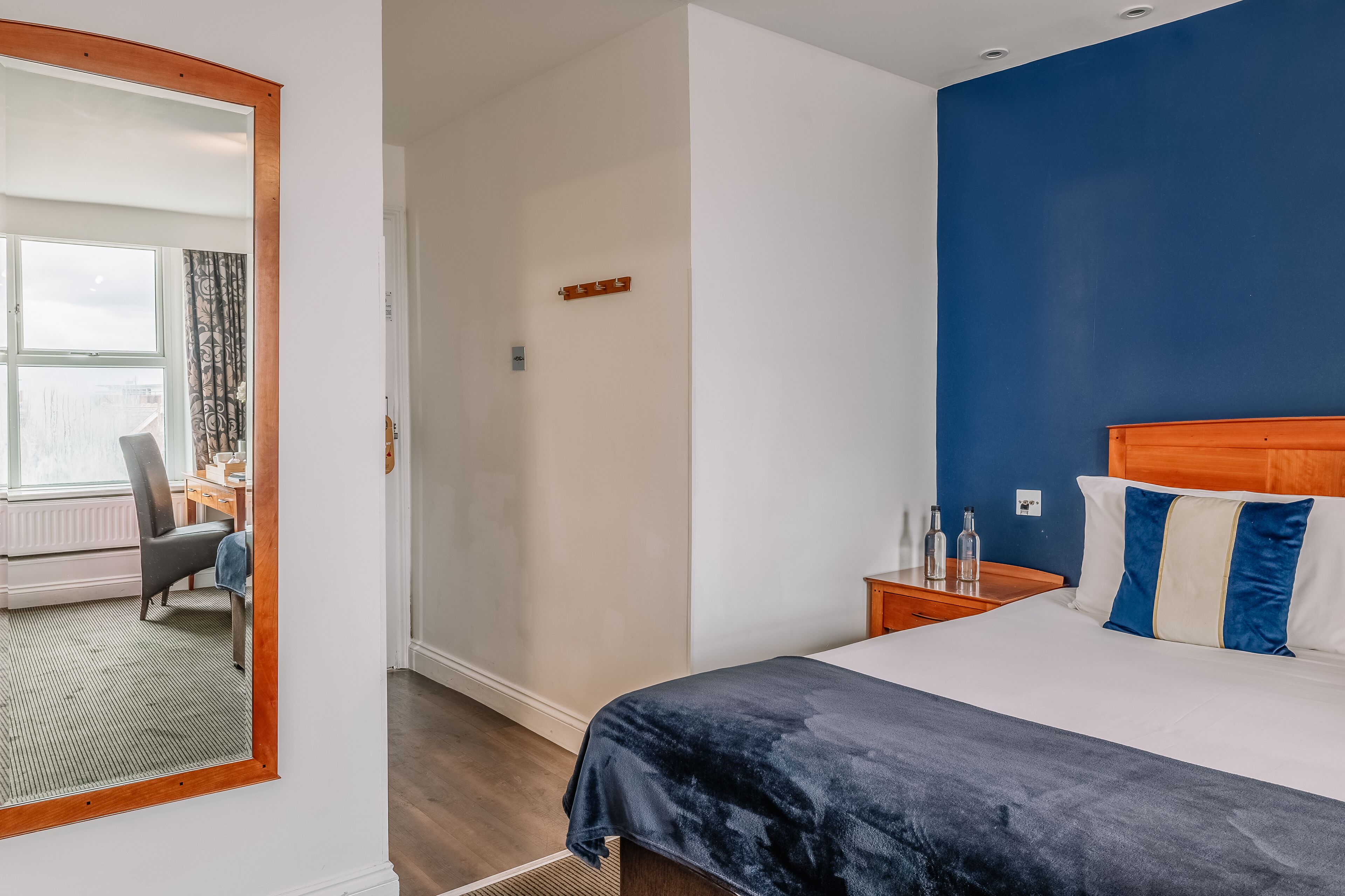 A hotel room with a large bed, a wooden headboard, a desk with a chair, and a view through a window with curtains.