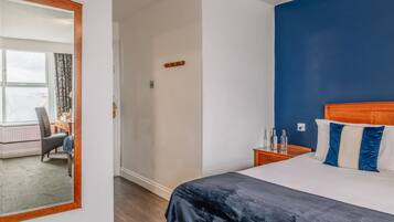 A hotel room with a large bed, a wooden headboard, a desk with a chair, and a view through a window with curtains.