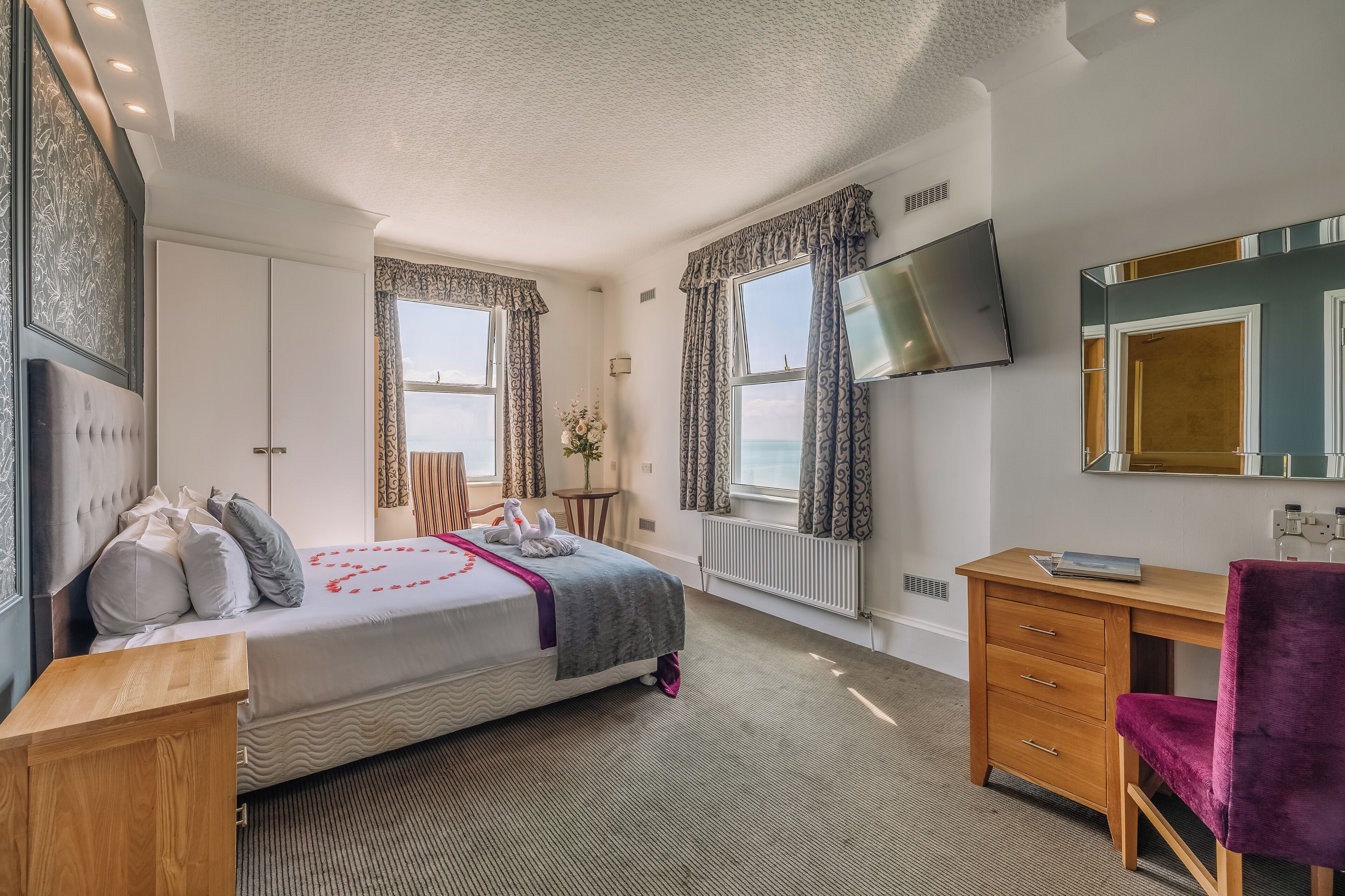 A hotel room with a bed, a desk, a chair, a TV, and a window with curtains.