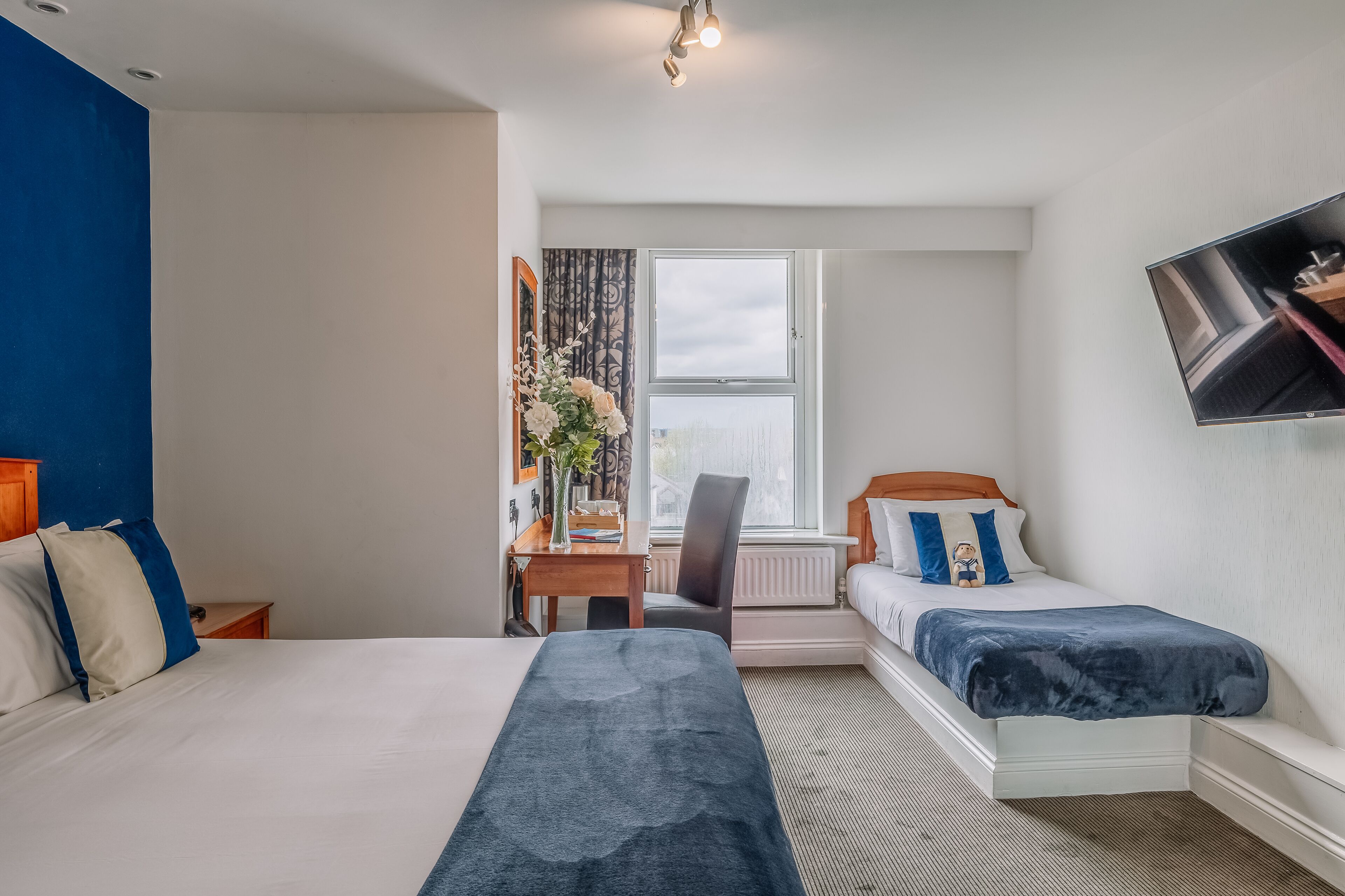 A hotel room with a bed, a desk, a chair, a TV, and a window with curtains.