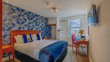 A hotel room with a large bed, a desk with a chair, a TV mounted on the wall, and a window with a view.