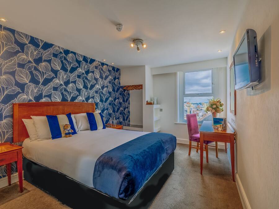 A hotel room with a large bed, a desk with a chair, a TV mounted on the wall, and a window with a view.