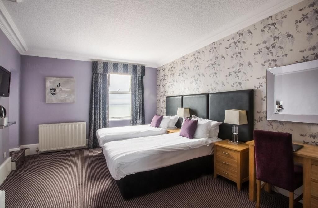 Ein Hotelzimmer mit zwei Betten, einem Schreibtisch, einem Stuhl, einem Fernseher und einem Fenster mit Vorhängen.