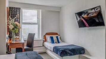 Un dormitorio con cama, escritorio, silla, ventana y televisor instalado en la pared.
