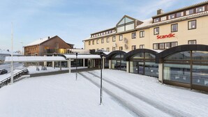 A hotel with a snow-covered ground, a covered outdoor seating area, and a large windowed facade. - Scandic Vadsø (Vadsø)